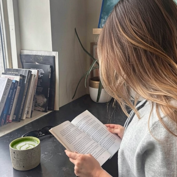 a woman reading a book with a bowl of matcha beside her, a moment of quiet focus